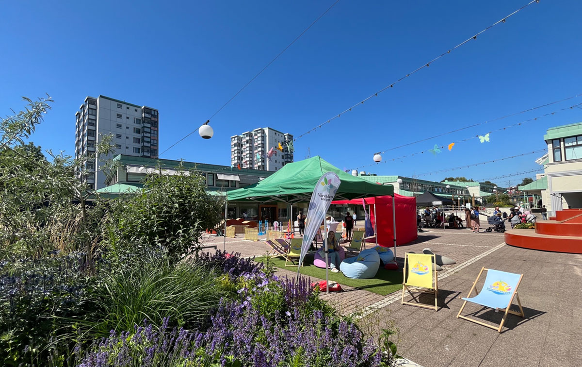 vvt-2024 Ungdomar som kopplar av i solstolar på Vårväderstorget. Blå himmel och grönska i förgrunden.